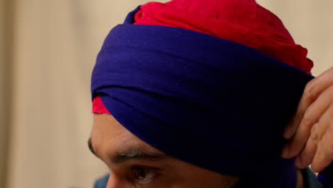 Close-Up-Studio-Shot-Of-Two-Sikh-Men-Tying-Fabric-For-Turban-Against-Plain-Background-1